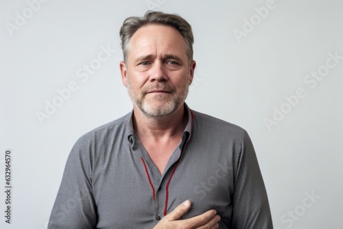 Medium shot portrait photography of a man in his 40s clutching his chest due to gastroesophageal reflux disease wearing a simple tunic against a white background  © Leon Waltz