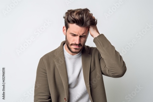 Lifestyle portrait photography of a man in his 20s pressing his temple due to a migraine wearing a chic cardigan against a white background 