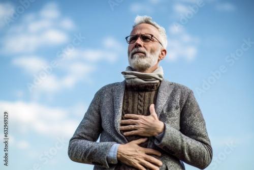 Medium shot portrait photography of a man in his 50s holding his stomach with discomfort from gastritis wearing a chic cardigan against a sky and clouds background 