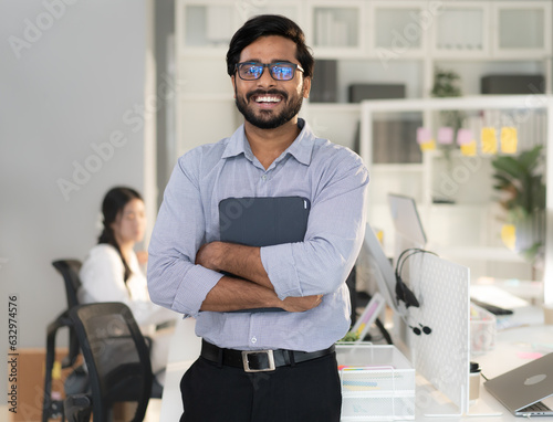 Friendly indian businessman standing arms crossed in workplace looking at camera smiling. Confident smart success entrepreneur, corporate boss work in office. Male india ethnic manager businessperson. photo