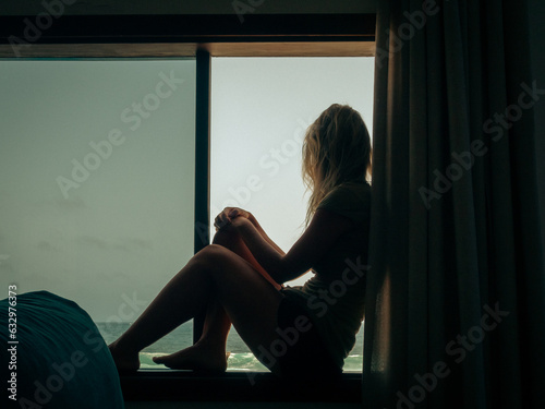 Silhouette of a woman looking at the sea from a window
