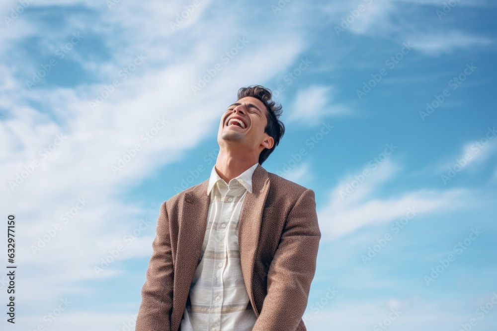 Lifestyle portrait photography of a man in his 20s wincing with pain and holding his lower back due to sciatica wearing a chic cardigan against a sky and clouds background 
