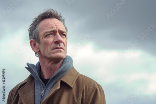 Medium shot portrait photography of a man in his 40s with a somber and deeply sad expression due to major depression wearing a chic cardigan against a sky and clouds background 