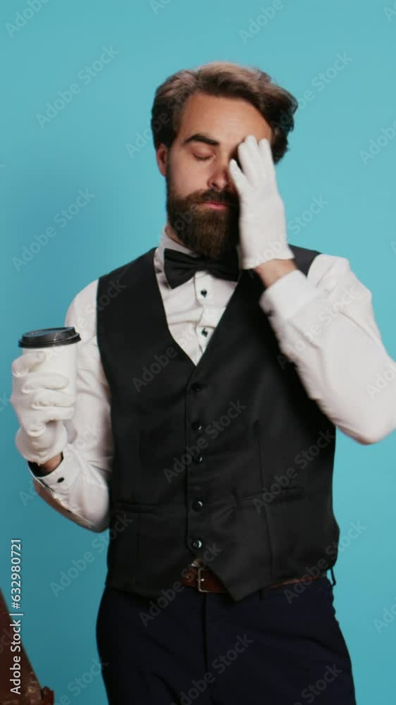 Vertical video Doorman holding coffee drink in studio, wearing white gloves and feeling confident working in hotel industry. Bellhop worker in suit and tie drinking beverage next to trolley bags. Vertical video Doorman holding coffee drink in studio, wearing white gloves and feeling confident working in hotel industry. Bellhop worker in suit and tie drinking beverage next to trolley bags.