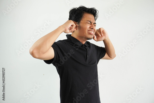 Angry young Asian man close his ears with fingers wearing black polo t shirt isolated on white background photo