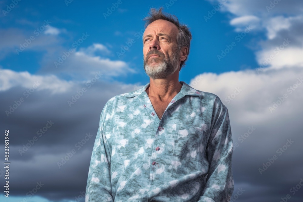 Medium shot portrait photography of a man in his 50s visibly in discomfort and fatigue from an autoimmune disease like lupus wearing a snuggly pajama set against a sky and clouds background Medium shot portrait photography of a man in his 50s visibly in discomfort and fatigue from an autoimmune disease like lupus wearing a snuggly pajama set against a sky and clouds background