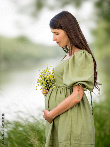 Caucasian Young Pregnant woman Tummy belly  summer green dress touching stomach field expecting a baby relaxing outside nature park lake rural Beautiful magic 8 months enjoying life glasses hat
