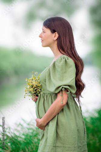 Caucasian Young Pregnant woman Tummy belly  summer green dress touching stomach field expecting a baby relaxing outside nature park lake rural Beautiful magic 8 months enjoying life glasses hat