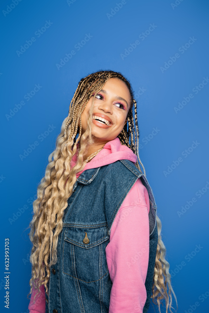 cheerful african american woman with dreadlocks and bold makeup looking away on blue background cheerful african american woman with dreadlocks and bold makeup looking away on blue background