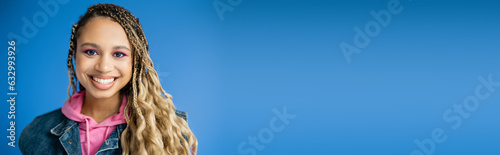 banner, joyful african american woman in pink hoodie and denim vest on blue background, dark skinned