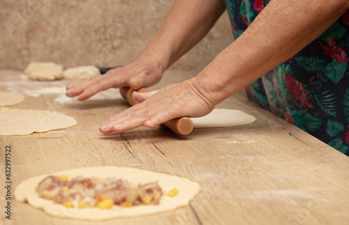 A woman rolls out the dough with a rolling pin on the table