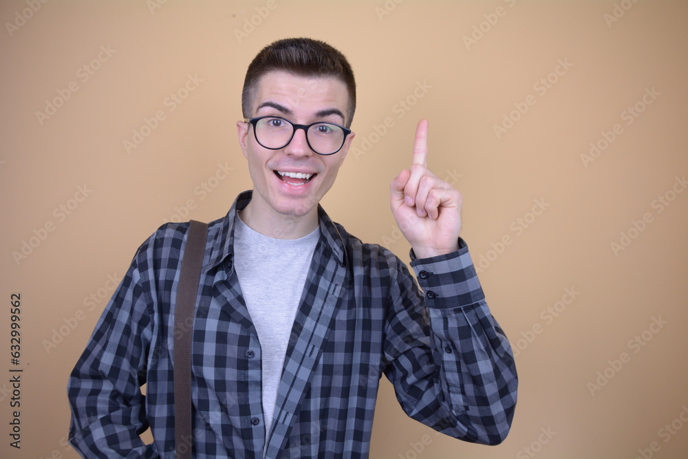 Smiling Student with Glasses Expressing a Brilliant Idea. Young Man in Plaind Shirt with a Genius Thought on Isolated Background. Smiling Student with Glasses Expressing a Brilliant Idea. Young Man in Plaind Shirt with a Genius Thought on Isolated Background.