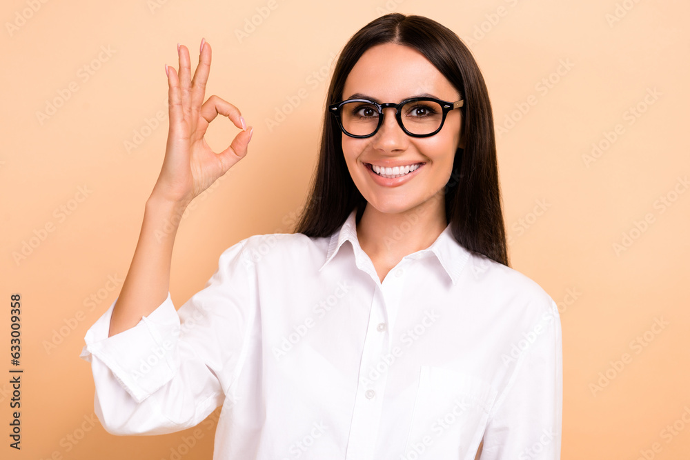 Photo of smiling confident lady wear white shirt spectacles smiling showing okey gesture isolated beige color background