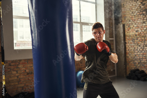 Best fighter. Young and strong man boxing in red gloves in a loft style gym.