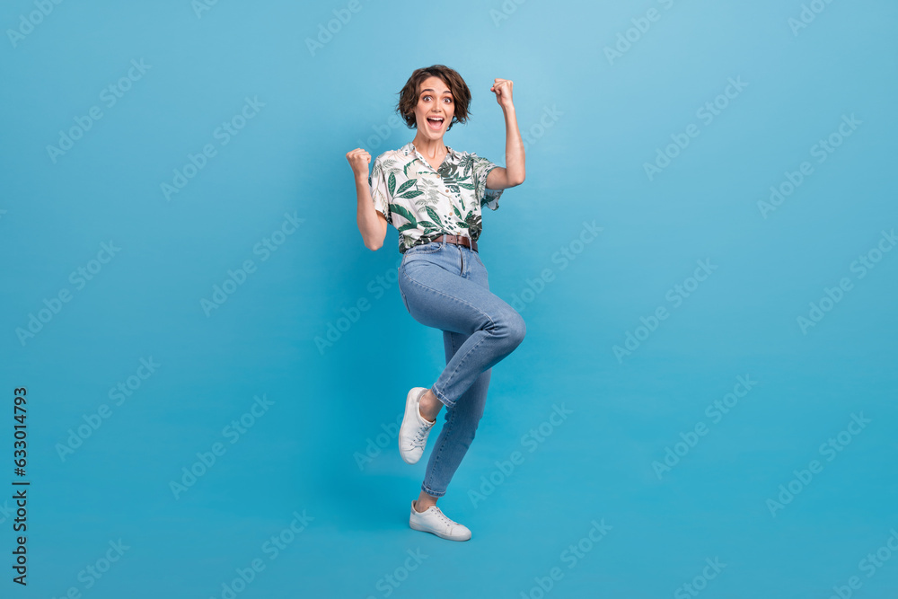 Full length photo of pretty lucky woman dressed print shirt screaming rising fists isolated blue color background Full length photo of pretty lucky woman dressed print shirt screaming rising fists isolated blue color background