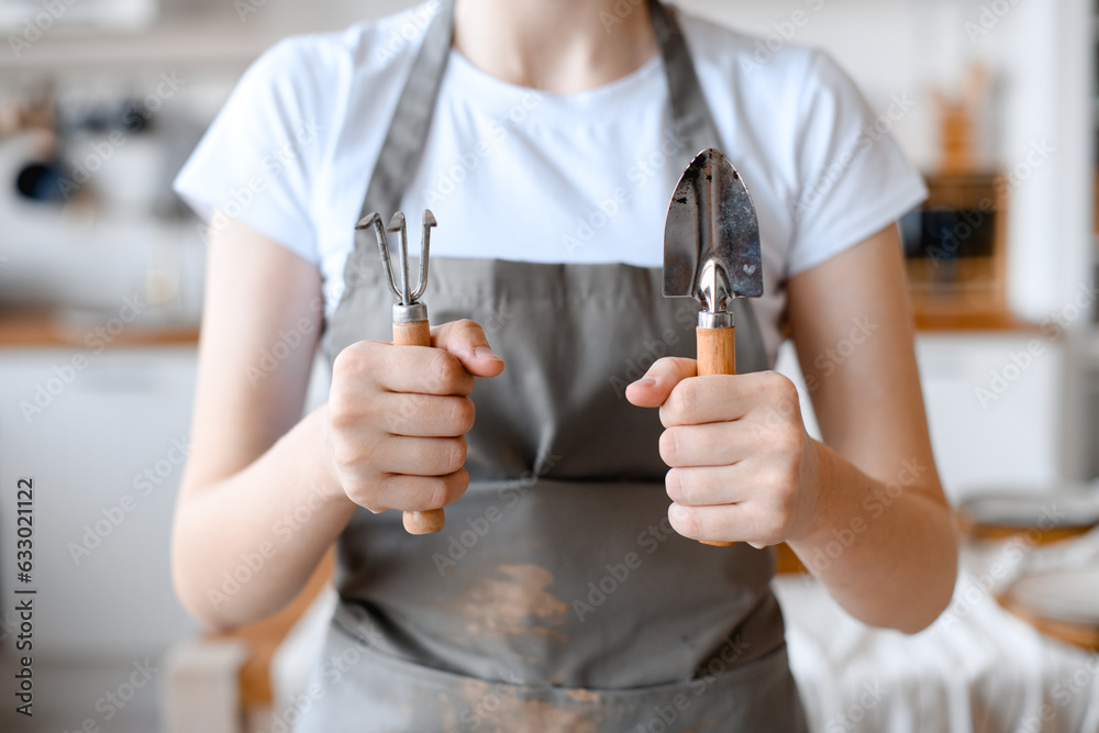 Fototapeta premium Woman gardener in grey apron holding garden utensils. Ready to work