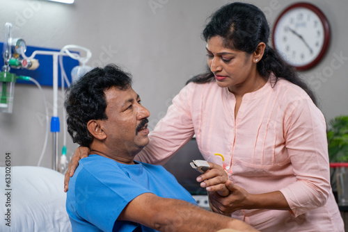 Caring Indian wife helping sick husband to get up from bed while admitted at hospital ward - concept of family assistance, Compassion and medical treatment. photo