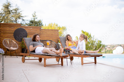 Family with a mother, father and daughter sitting on the deck chairs by the swimming pool © BGStock72
