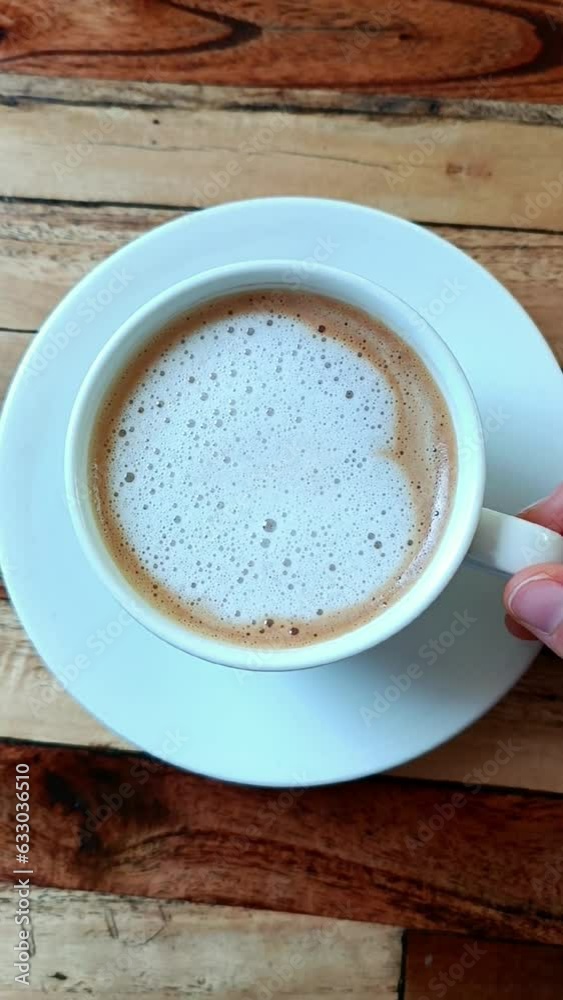 A view of a hand moves a white cup with a camuchino view from above. A lot of coffee for breakfast A view of a hand moves a white cup with a camuchino view from above. A lot of coffee for breakfast