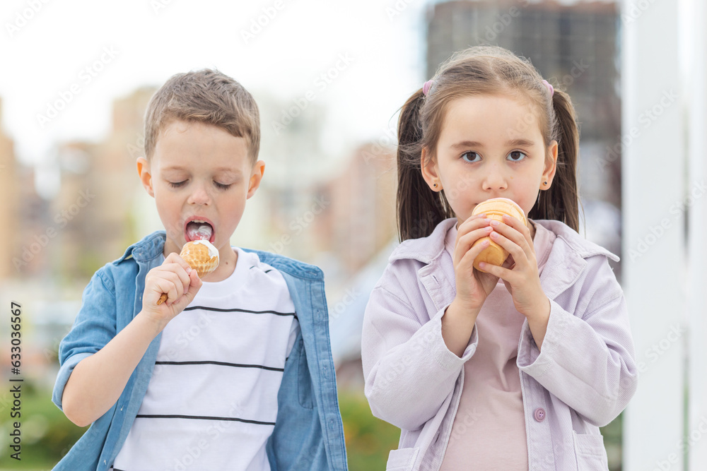 Two kids boy and girl eating ice cream outdoor on the street. Ice cream in a waffle cone. Two kids boy and girl eating ice cream outdoor on the street. Ice cream in a waffle cone.