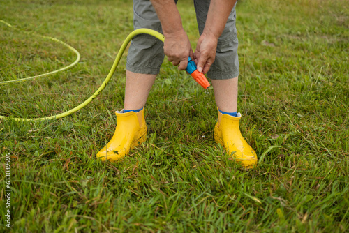 Washing of rubber boots. Close-up of a woman's hands washes yellow rubber boots from mud with a garden hose in the garden after working in the ground
