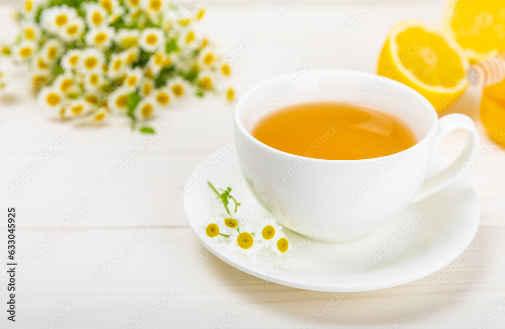 Chamomile tea on a white table. Delicious tonic, soothing and relaxing chamomile tea with chamomile flowers, honey and lemon. Herbal tea for immunity. Close-up.Place for text.Copy space. Chamomile tea on a white table. Delicious tonic, soothing and relaxing chamomile tea with chamomile flowers, honey and lemon. Herbal tea for immunity. Close-up.Place for text.Copy space.