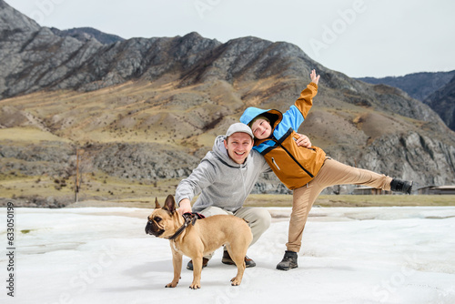 Smiling man with his son and dog enjoy a walk in the mountains among the snow