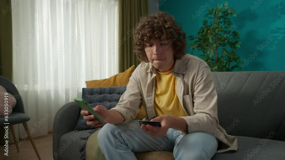 Young man sitting on the sofa in the living room with a smartphone and credit card in hands Young man sitting on the sofa in the living room with a smartphone and credit card in hands