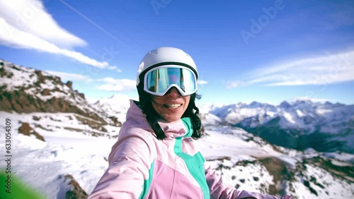 Smiling woman blogger vlogger standing on top mountain talking with camera recording video. Female skyer in protective clothing helmet goggles. Create content for blog, vlog. Winter sport resort. photo