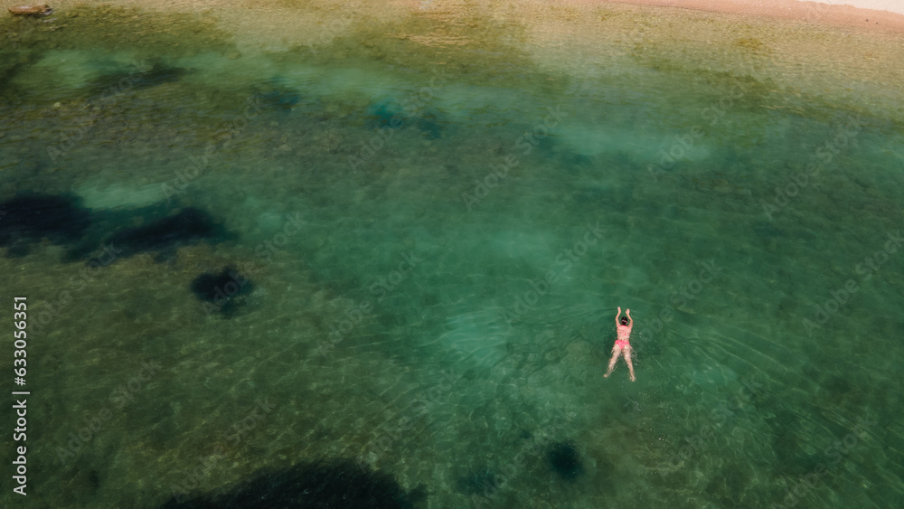 Aerial top view of woman in sea pool water from above, tropical vacation holiday concept. Mediterranean sea. Aerial seascape with woman, clear blue water, waves in summer. Transparent water. 