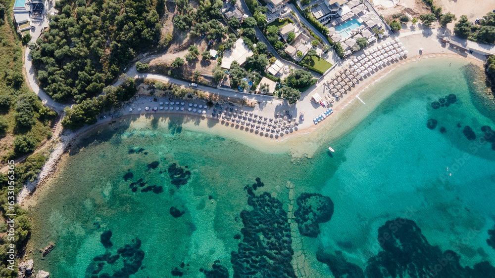 Aerial view of umbrellas, palms on the sandy beach of  at sunset. Summer holiday in Syvota, Greece. Tropical landscape with palm trees, parasols, white sand, blue water, waves. Top view