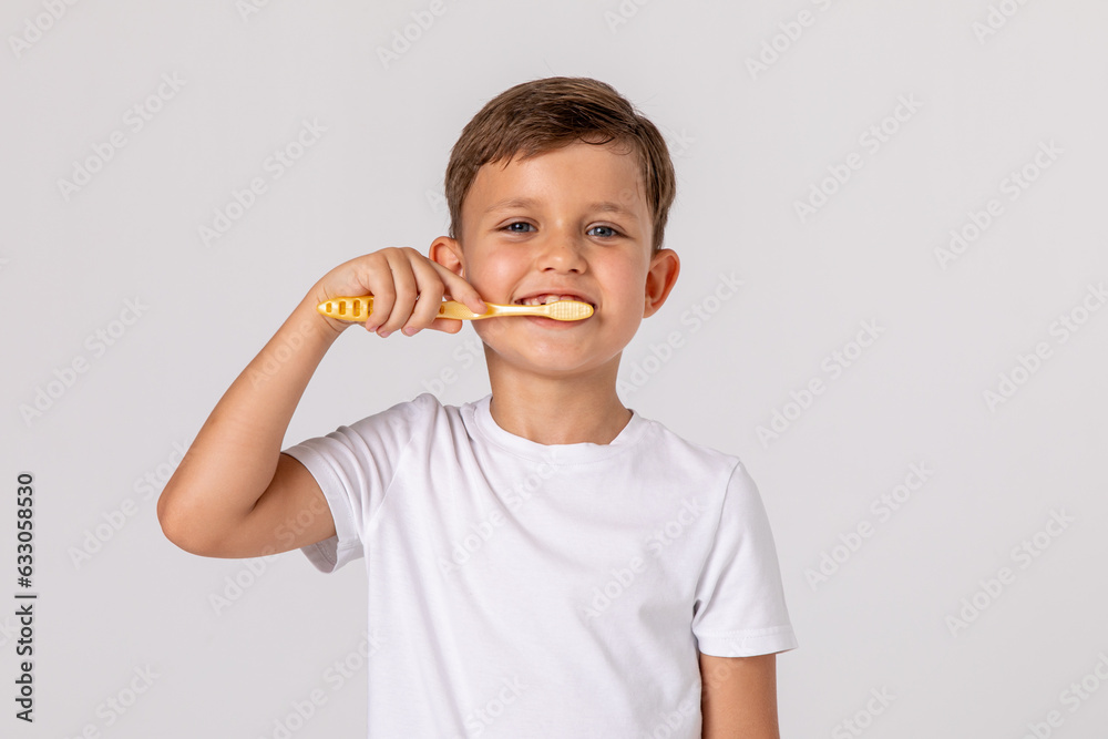 Morning concept. Close-up portrait of a happy little boy with toothbrush on white background. A child in a white T-shirt brushes his teeth on his own. Space for text Morning concept. Close-up portrait of a happy little boy with toothbrush on white background. A child in a white T-shirt brushes his teeth on his own. Space for text
