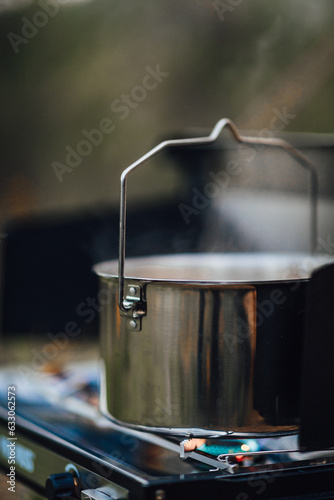 Boiling water in a pot on a portable gas camping stove. Preparing a meal outdoors near the tent on a camp ground. Nomad life traveling, simple slow living, summer escape adventure close to nature 