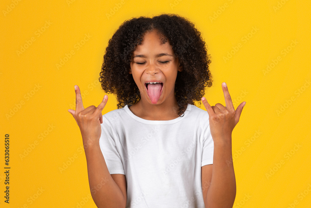 Glad excited teenage black pupil girl in white t-shirt show tongue, make goat gesture with hands Glad excited teenage black pupil girl in white t-shirt show tongue, make goat gesture with hands