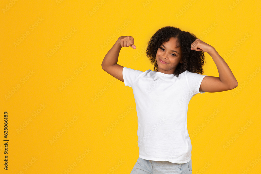Φωτογραφία Positive teenage black pupil girl in white t-shirt shows biceps muscles