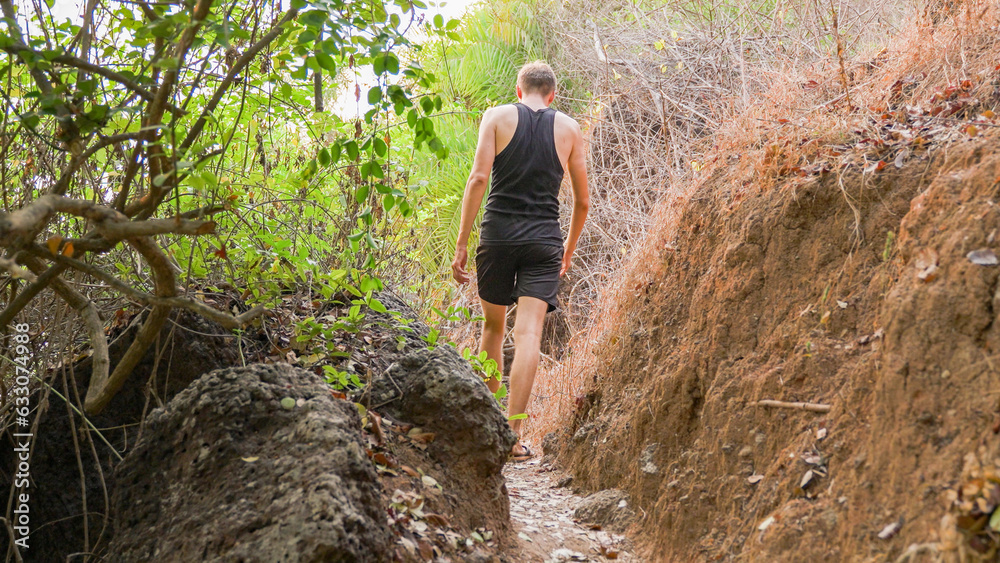 young man dressed in black walking along a pathway in the tropics