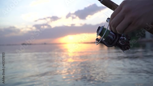 a fisherman spins a fishing rod reel in the sea against the backdrop of sunset