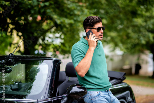 Handsome man standing next to his convertible car and using smartphone