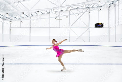 Young woman in pink dress figure skating at ice rink photo