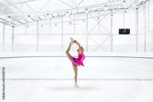 Young woman in pink dress figure skating at ice rink photo