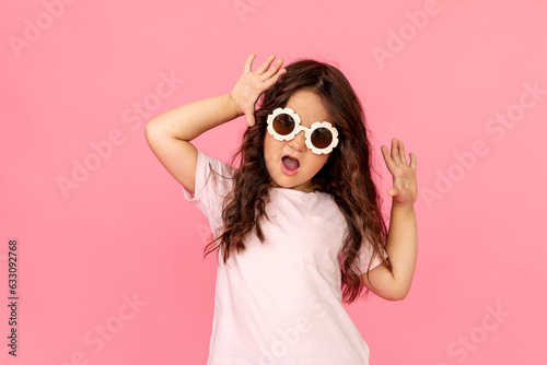 Portrait of a funny girl in sunglasses laughing at camera on a pink background. Copy space. Studio shot. Happy childhood. Education.