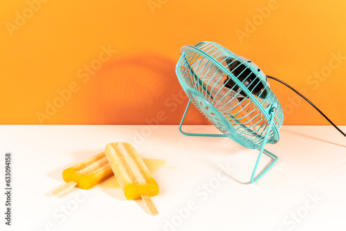 Mango orange ice lollies cooling with a blue little fan on white and orange background photo