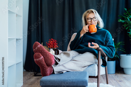 Fotografie Middle aged woman relaxing with pumpkin shaped cup of hot drink in scandy style hygge interior home with fall mood decor