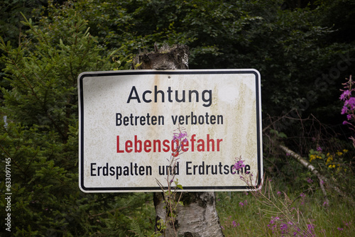 A german warning sign with a text that translates to "warning, illegal to enter. danger of death, rock slides and steep cliffs". a sign near a mining area.