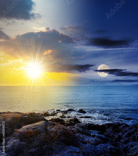 sea wave attacks the boulders of rocky shore with sun and moon at twilight. day and night time change concept. mysterious seascape scenery in morning light