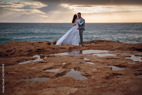 The newlyweds pose in wedding clothes on the rocks by the sea. Beautiful young couple tenderly embracing. Newlyweds wedding on the island