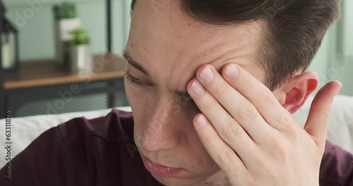 Caucasian man is depicted sitting on the sofa in the living room with a look of sadness on his face. His eyes reflect a deep sense of melancholy, and his posture conveys a feeling of heaviness.