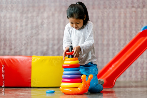Niña latina feliz  jugando con pequeña torre de aros de colores. Entretenimiento interior. Motricidad photo