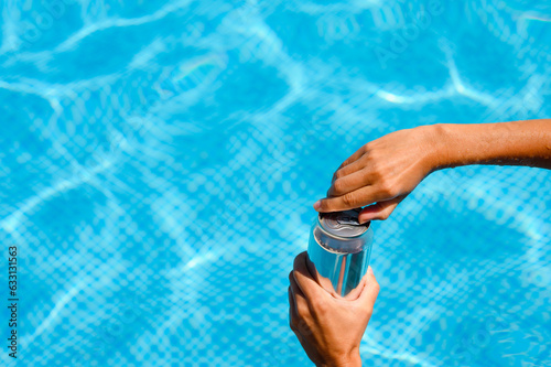 Close-up of a girl opens a drink in the pool. Summer vacation concept. Thirst on a hot summer day