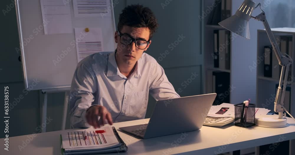 Dedicated businessman remains at his office desk, diligently engaged in his work. With a calculator in hand and surrounded by papers, he meticulously crunches numbers and analyzes data. Dedicated businessman remains at his office desk, diligently engaged in his work. With a calculator in hand and surrounded by papers, he meticulously crunches numbers and analyzes data.